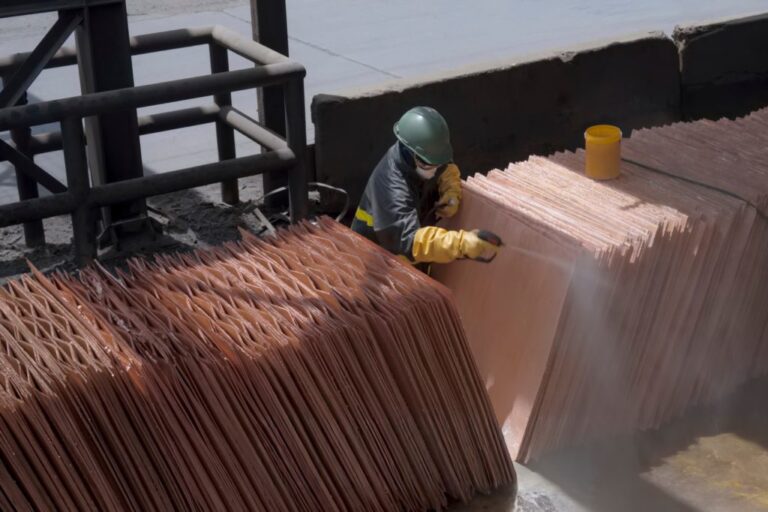 Worker inspecting stacks of refined copper cathode sheets at a metals plant